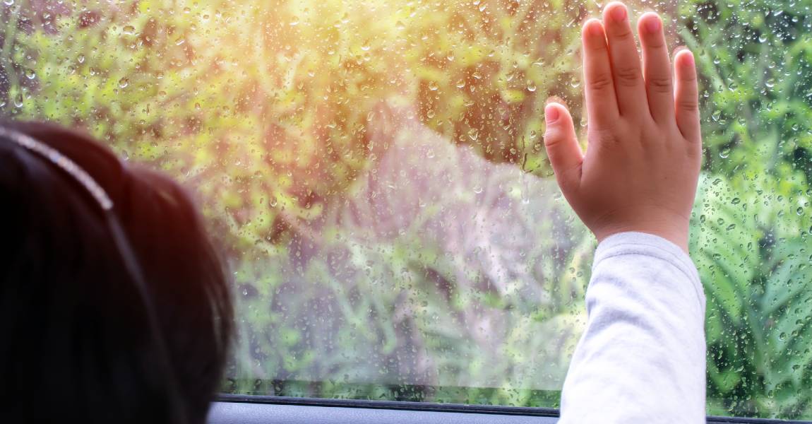 girl in car with hand on window looks at falling rain