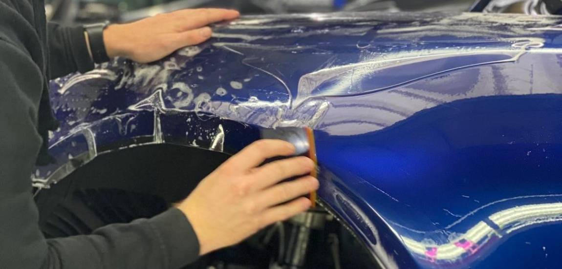 man applying paint protection film on blue car