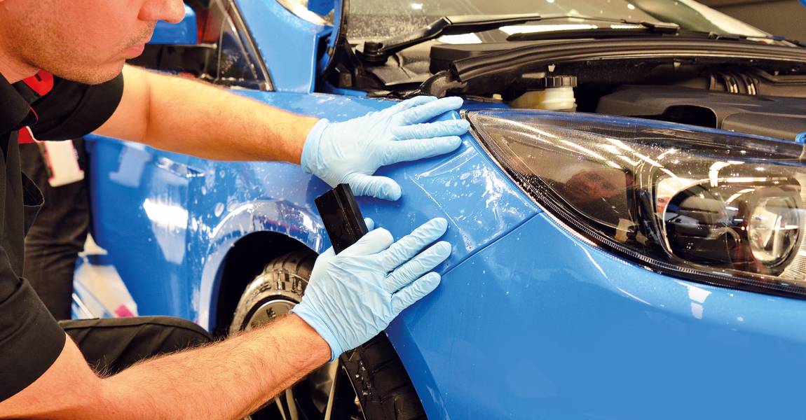 man installing paint protection film on blue car