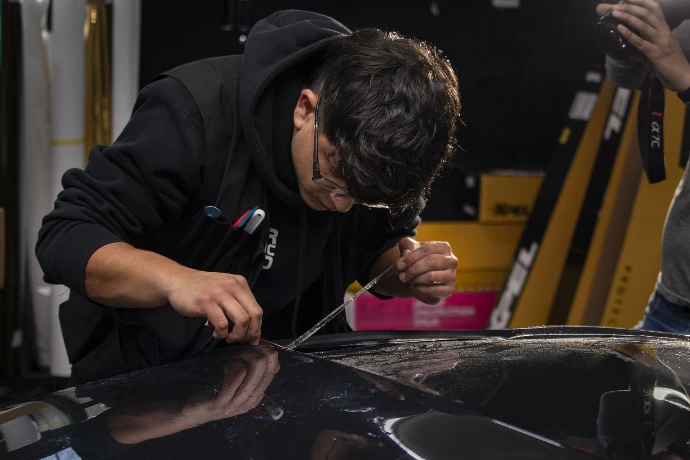 Professional PPF installer carefully cutting and fitting paint protection film to the hood of a 2018 Ford Shelby GT350