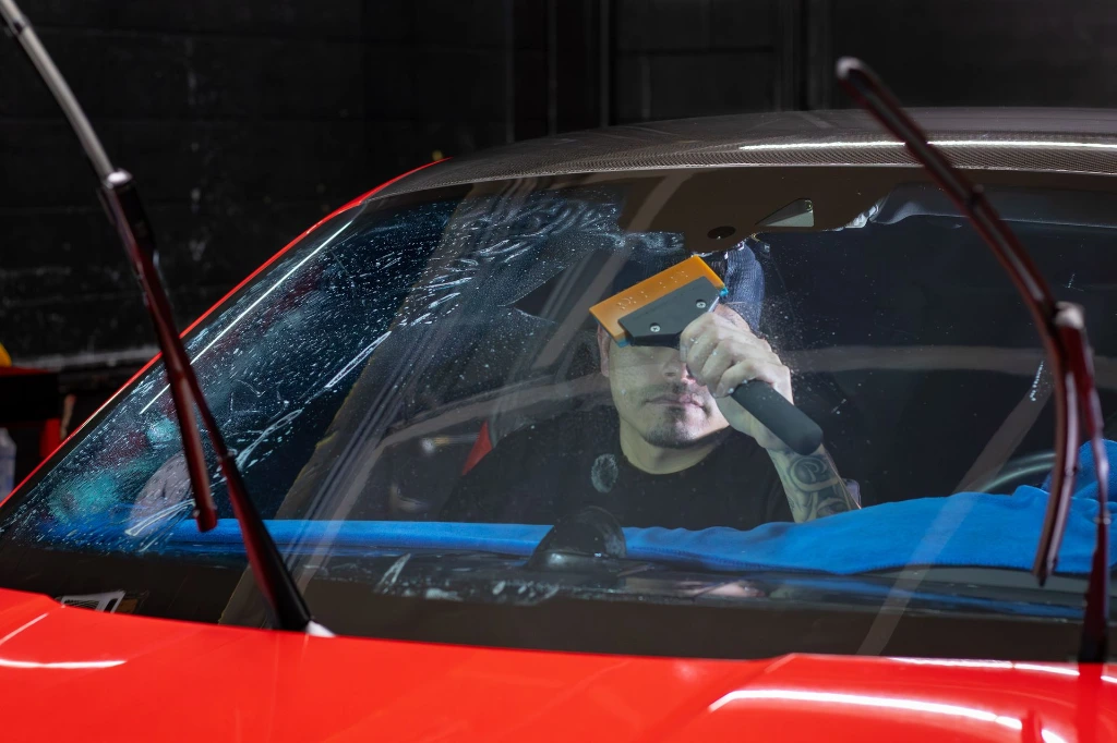 Technician applying lightly tinted window film to the windshield of a 2024 Porsche 911 Carrera GTS for heat and glare reduction