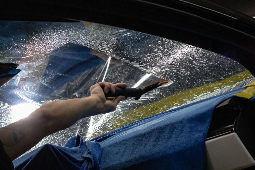 Technician applying lightly tinted window film to the inside of the windshield of a 2024 Porsche 911 Carrera GTS for heat and glare reduction