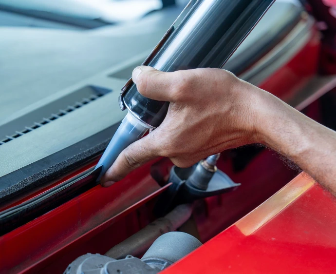 Professional windshield installer applying adhesive to a vehicle before windshield installation