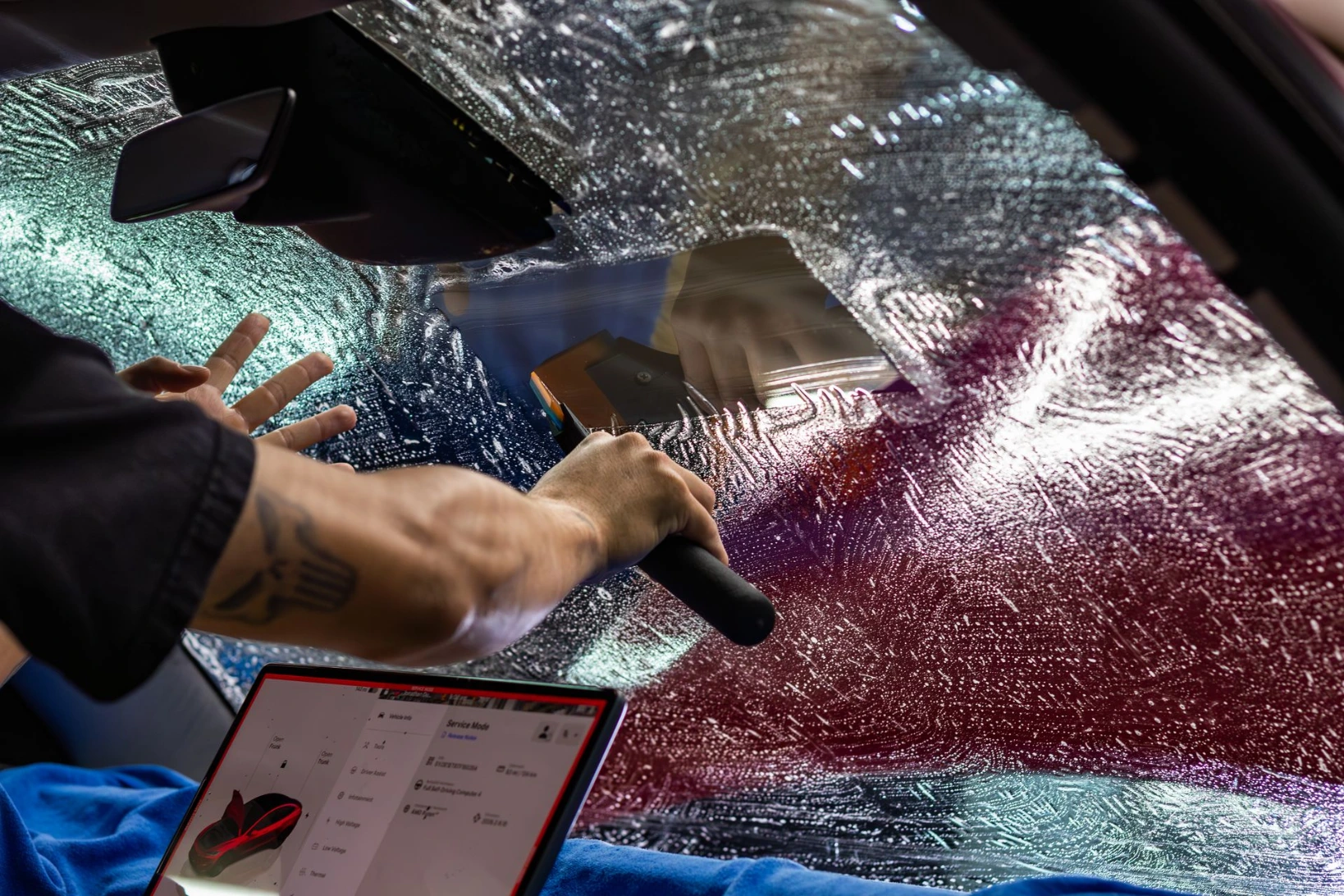 Squeegeeing slip solution on a windshield installation of ceramic film on a red Tesla